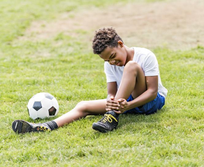 young boy holding ankle outside next to soccer ball