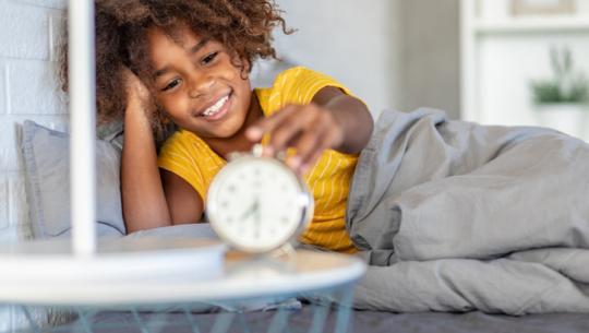 child in bed looking at clock