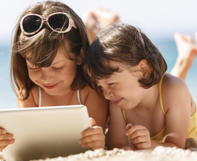two young girls on beach looking at digital tablet