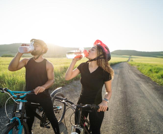 man and woman outside on bicycles drinking water
