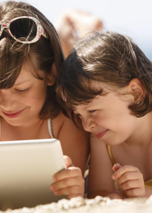 two young girls on beach looking at digital tablet